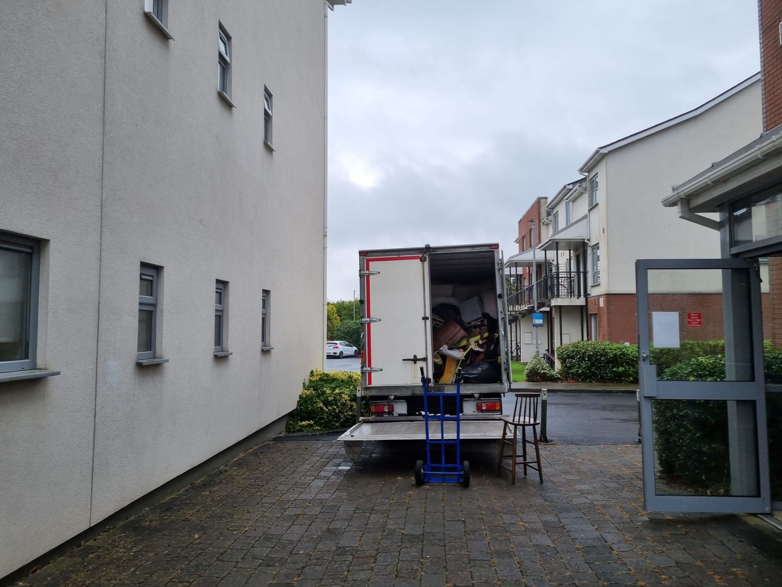 Our clearance van at the entrance of an apartment block, with a hand truck and a chair waiting to be loaded