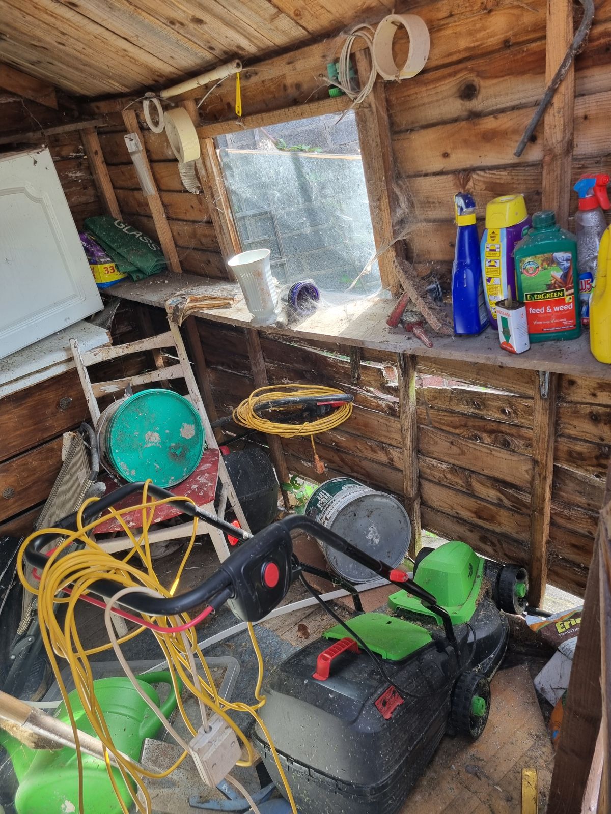 Inside a garden shed with a lawnmower, hoses and garden tools